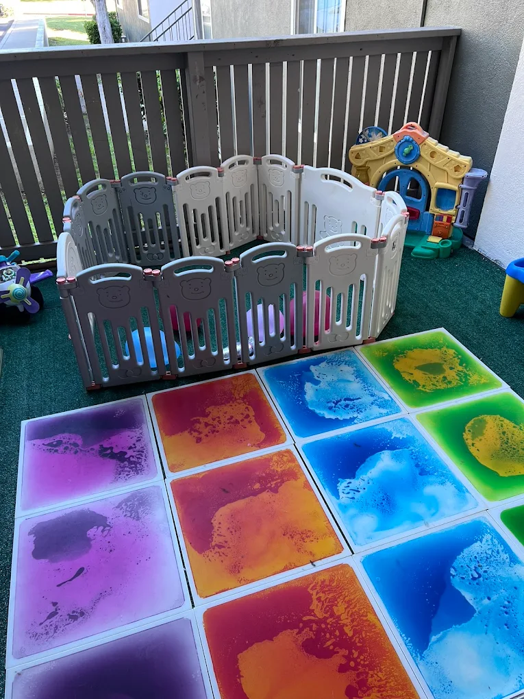 Fenced outdoor balcony play area with a playpen, sensory floor tiles and playhouse